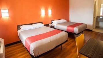 Una habitación de hotel con dos camas, suelo de madera y una mesita.
