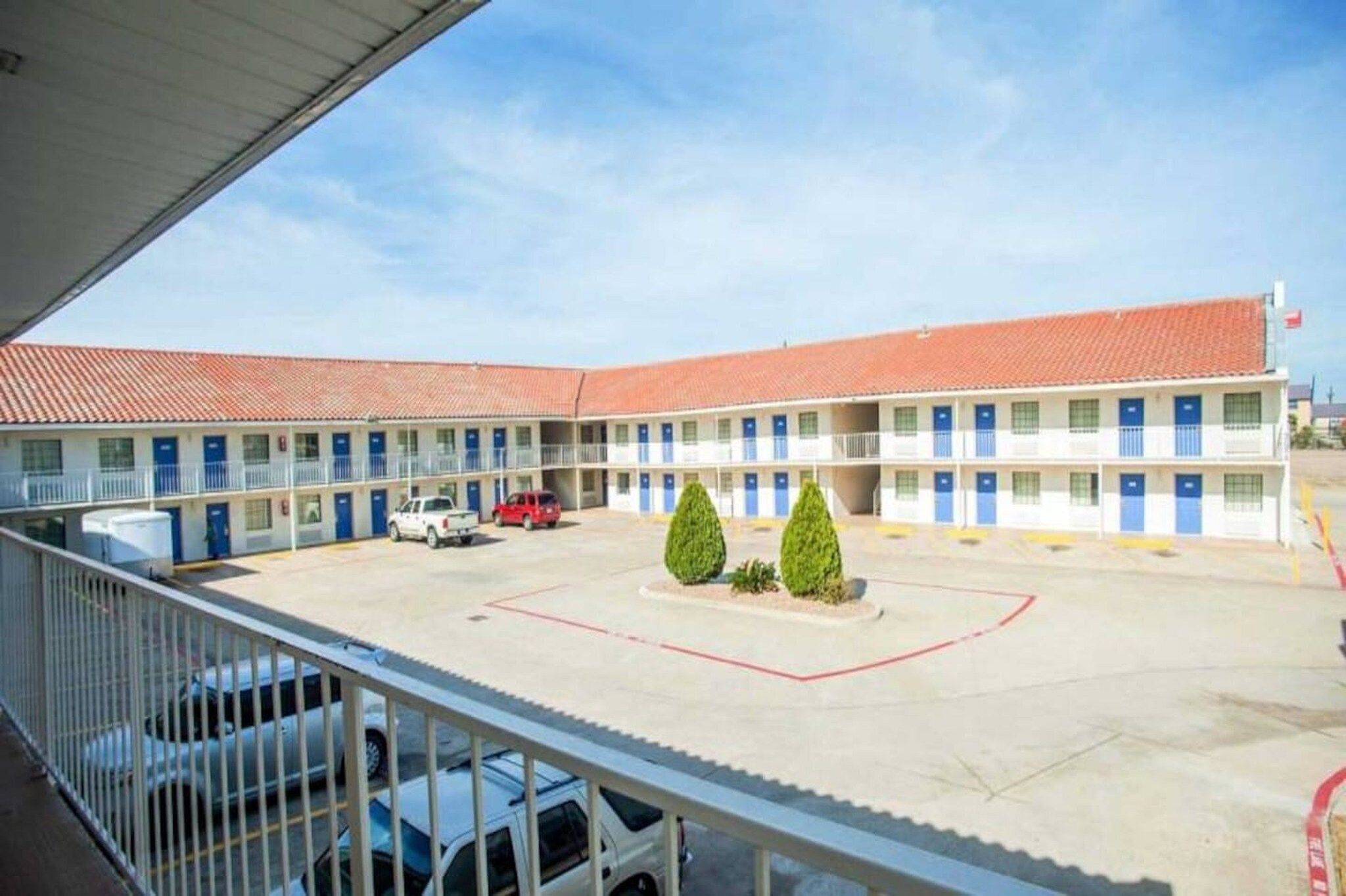 A motel with a central courtyard, multiple rooms with blue doors, and a red car parked in the lot.