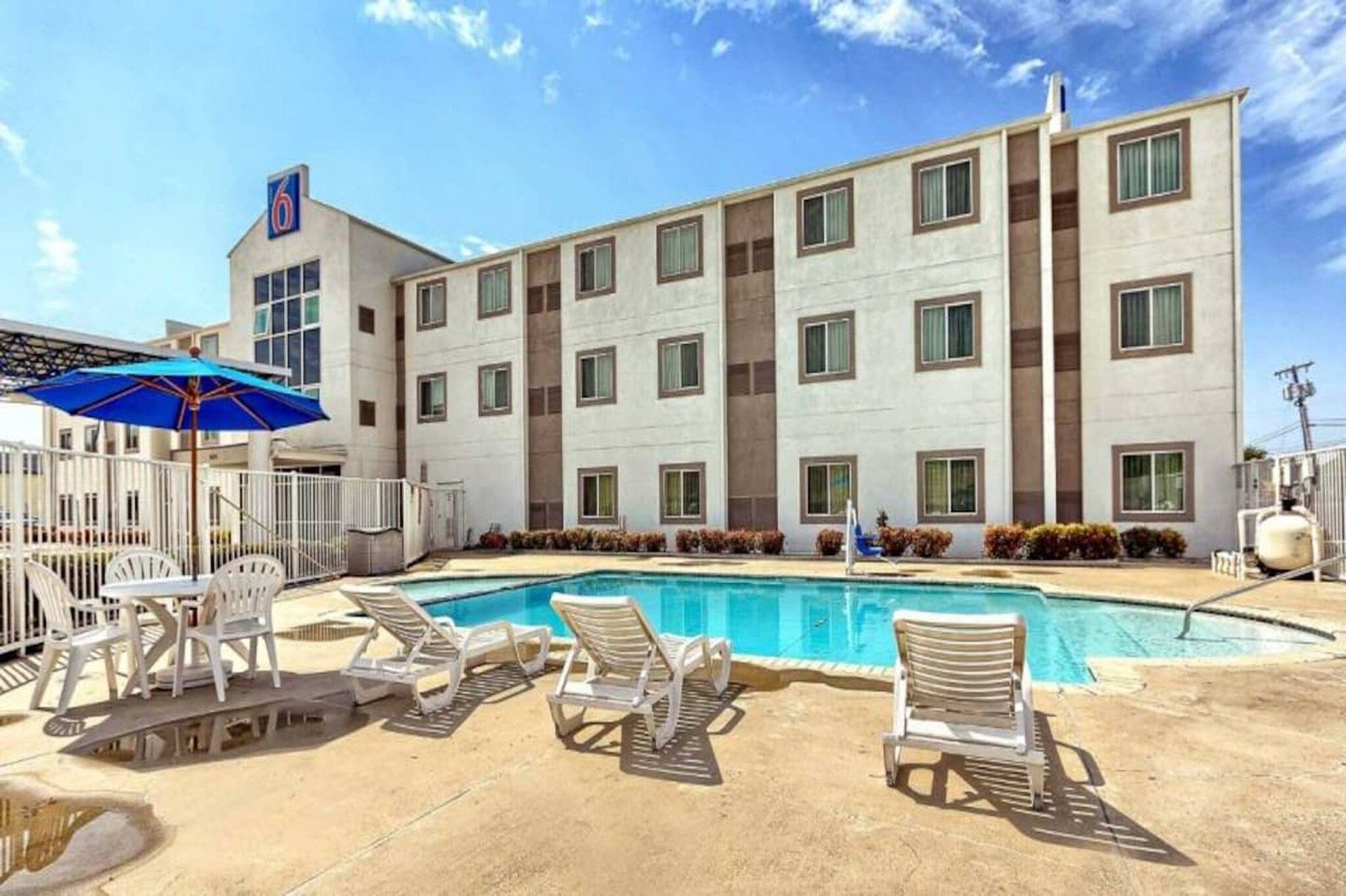 Un edificio de hotel con piscina, sillas de descanso y una sombrilla azul.