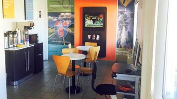 Un café avec un comptoir, des chaises et des tables. Il y a des affiches au mur et un ordinateur posé sur un support.