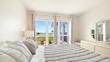 A bedroom with a large bed, a bedside table, a mirror, and a view of a green landscape through a sliding glass door.