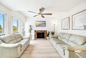 A living room with two beige sofas, a fireplace, a ceiling fan, and a large window.