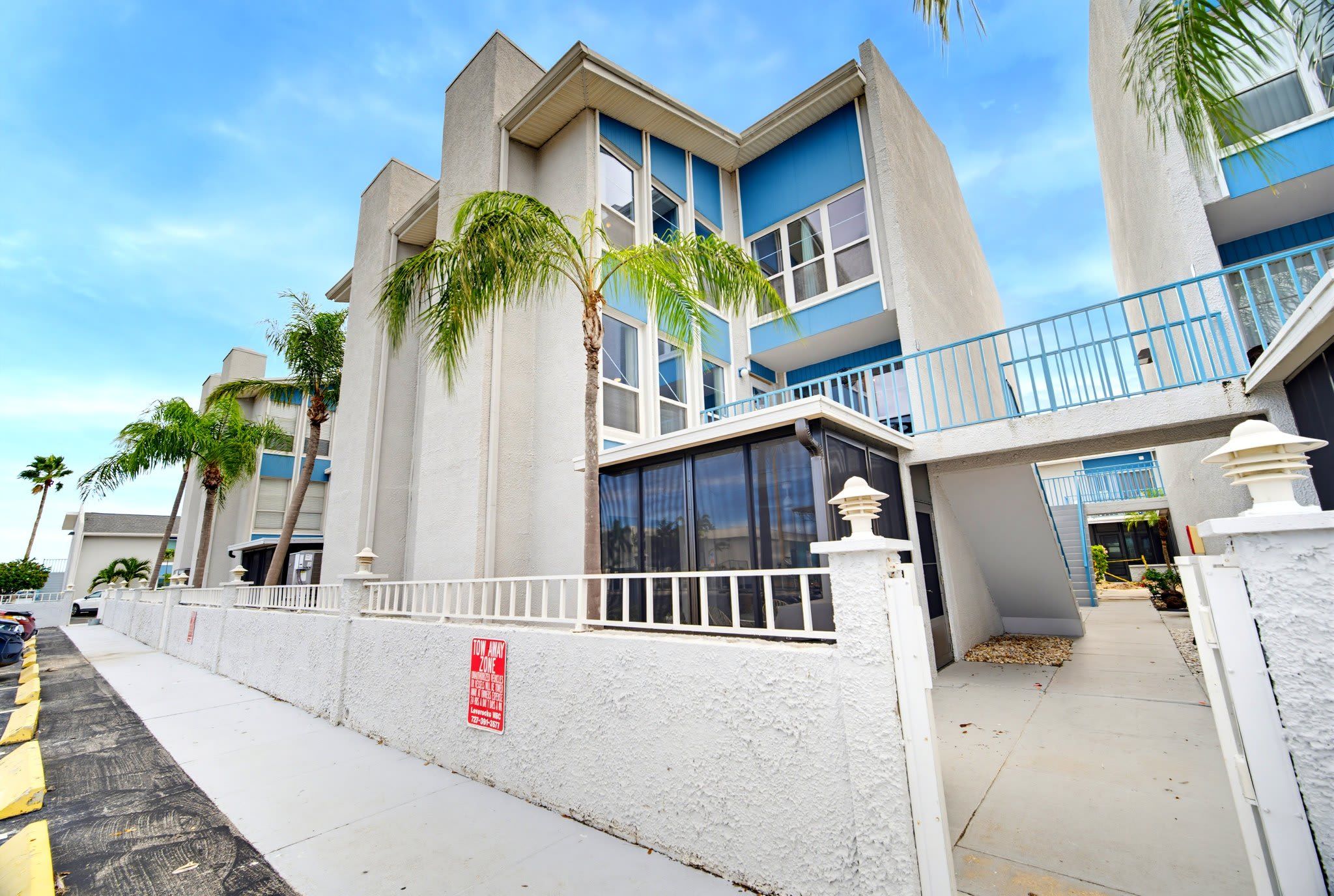 Un edificio residencial de varios pisos con balcones, una entrada con portones y palmeras.