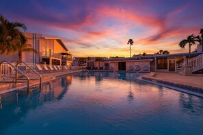 A swimming pool with a sunset view, a building with a balcony, and palm trees. - Walk to Beach & Heated Pool - Madeira Beach 2BR (Madeira Beach)