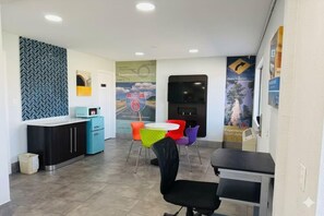 Een hotel receptie met een balie, een kleine kitchenette, kleurrijke stoelen en een groot poster aan de muur.