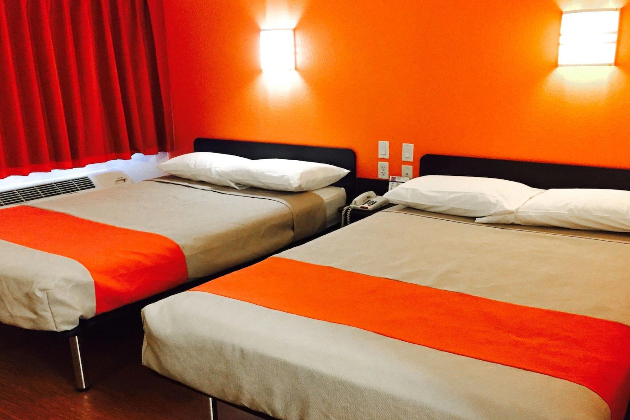 Een hotelkamer met twee bedden, elk met een wit kussen en een beige deken.