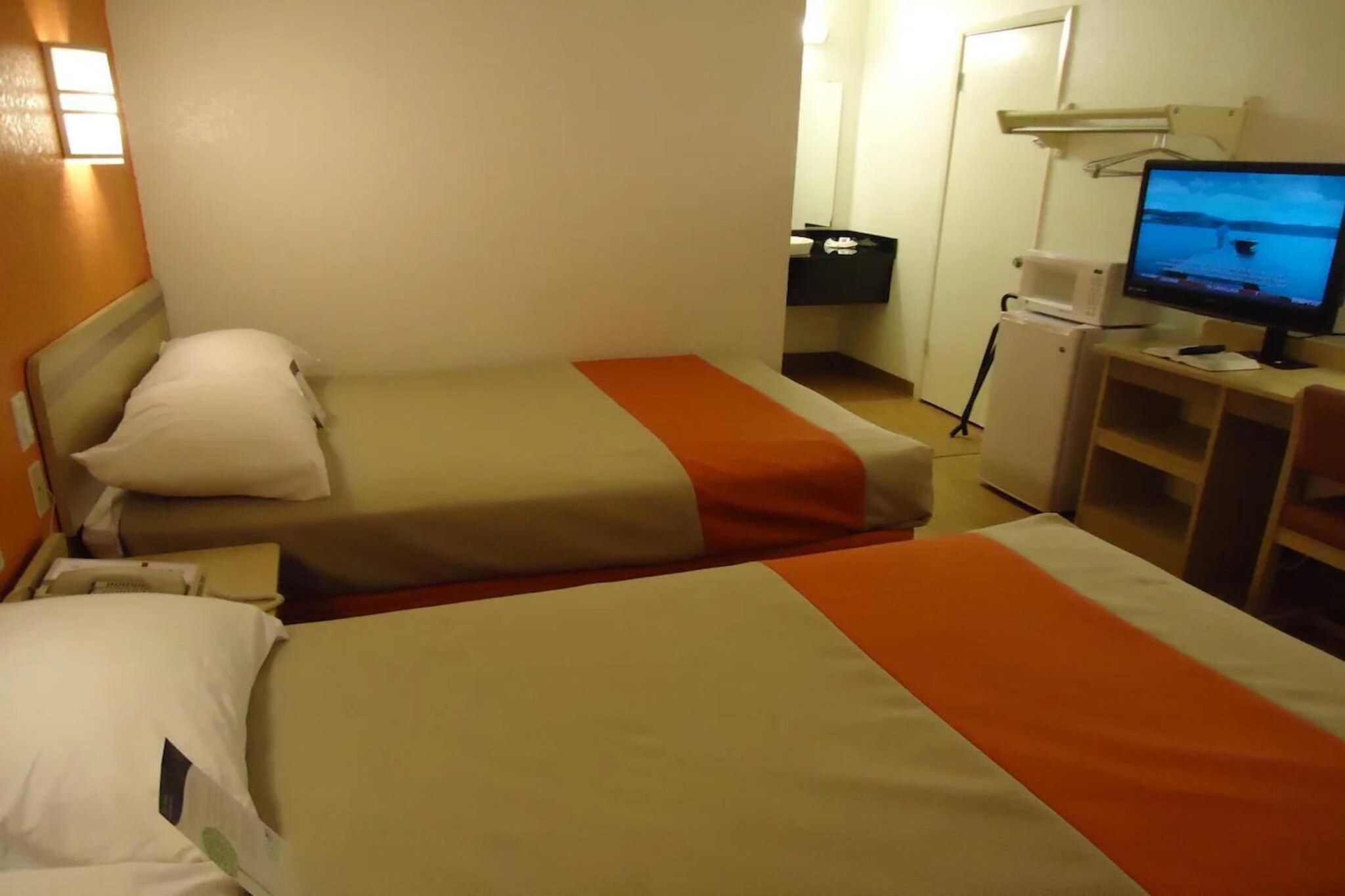 Une chambre d’hôtel avec deux lits, un bureau avec un ordinateur et une télévision.