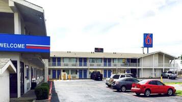 A motel with a 'WELCOME' sign, a '6' sign, and multiple cars parked in the lot.
