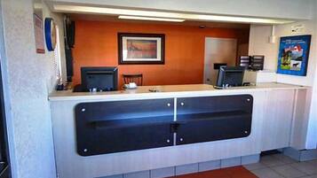 A reception desk with two computer monitors, a framed picture on the wall, and a poster on the right.