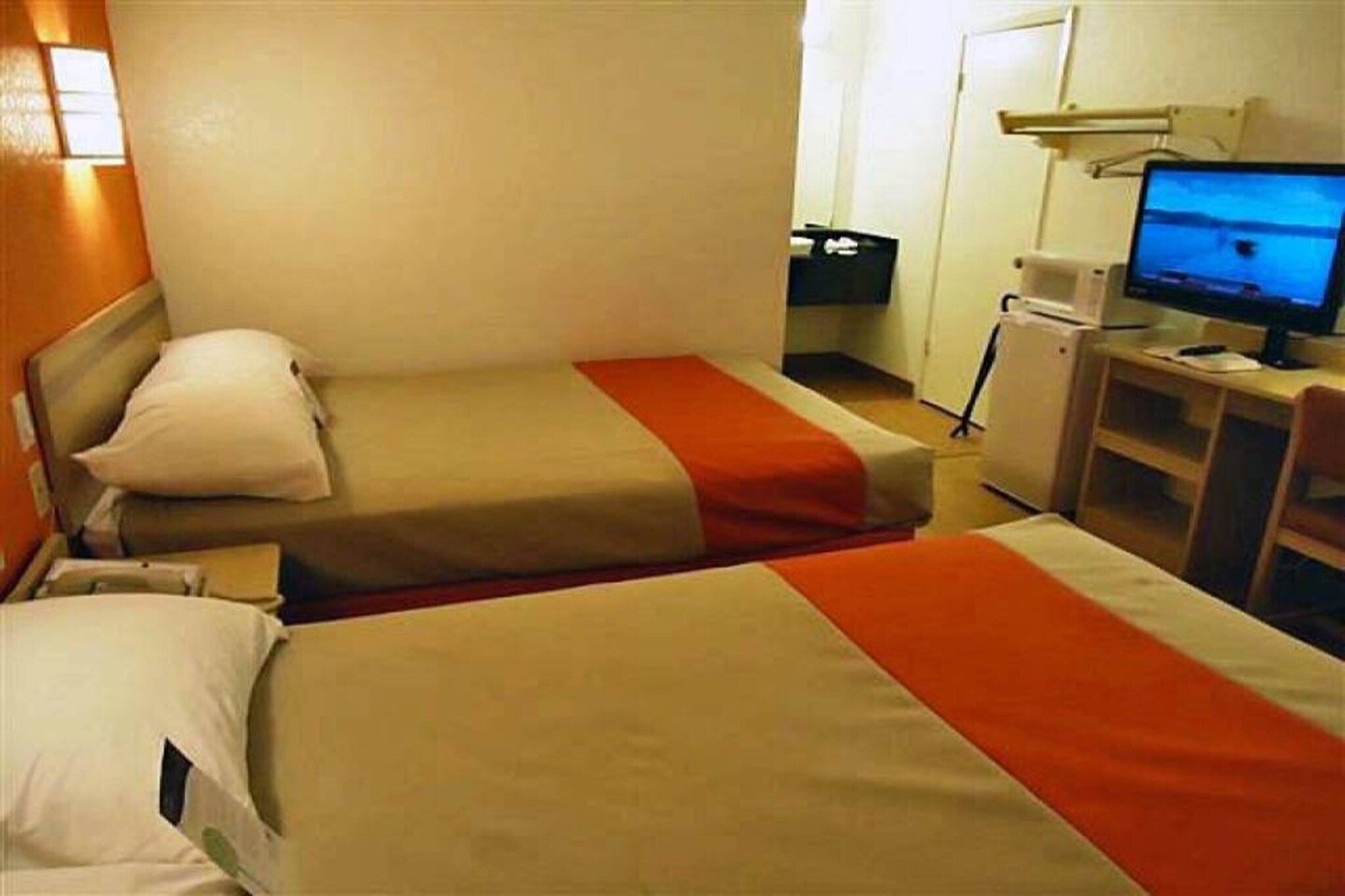 A hotel room with two beds, a desk with a computer, and a television.