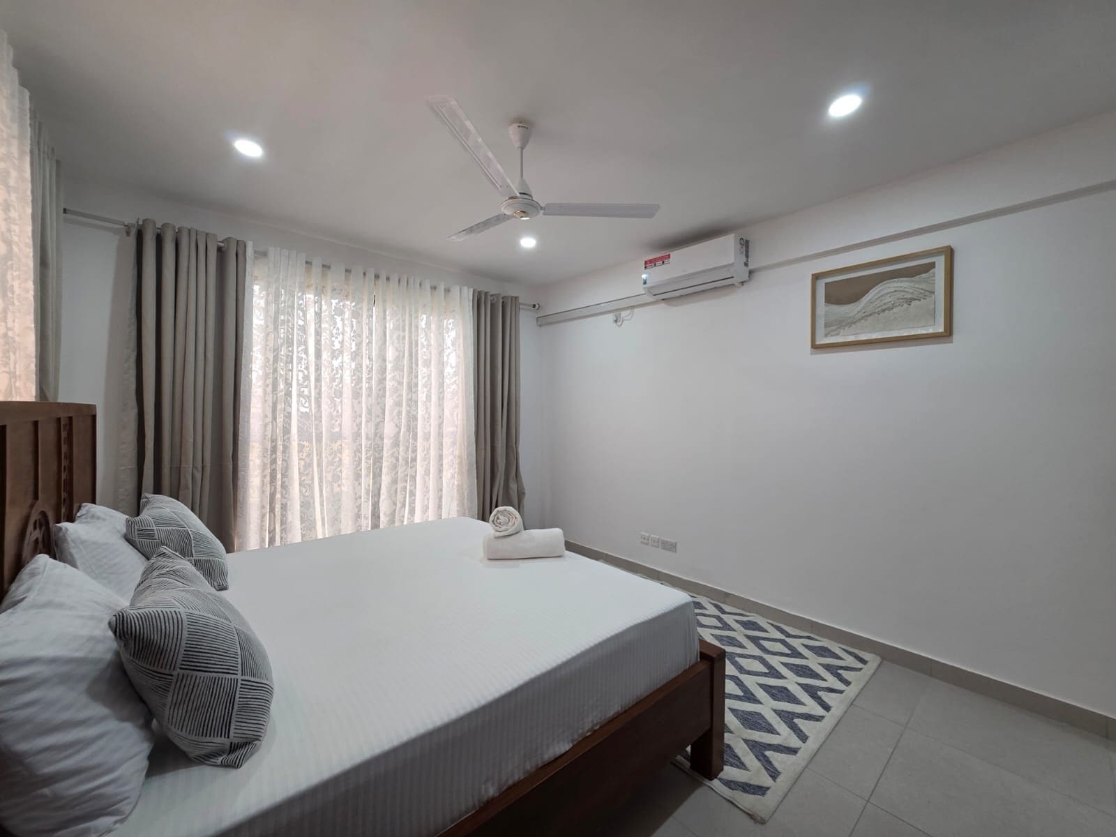 A bedroom with a bed, a ceiling fan, a window with curtains, and a framed picture on the wall.