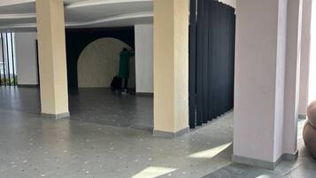 Ruime binnenruimte met een hoge plafond, grote pilaren en een persoon zittend in een half afgesloten ruimte.