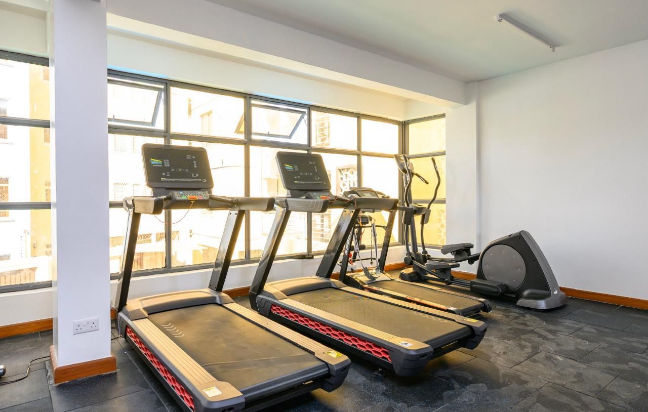 A gym with treadmills and an elliptical machine, large windows, and a tiled floor.