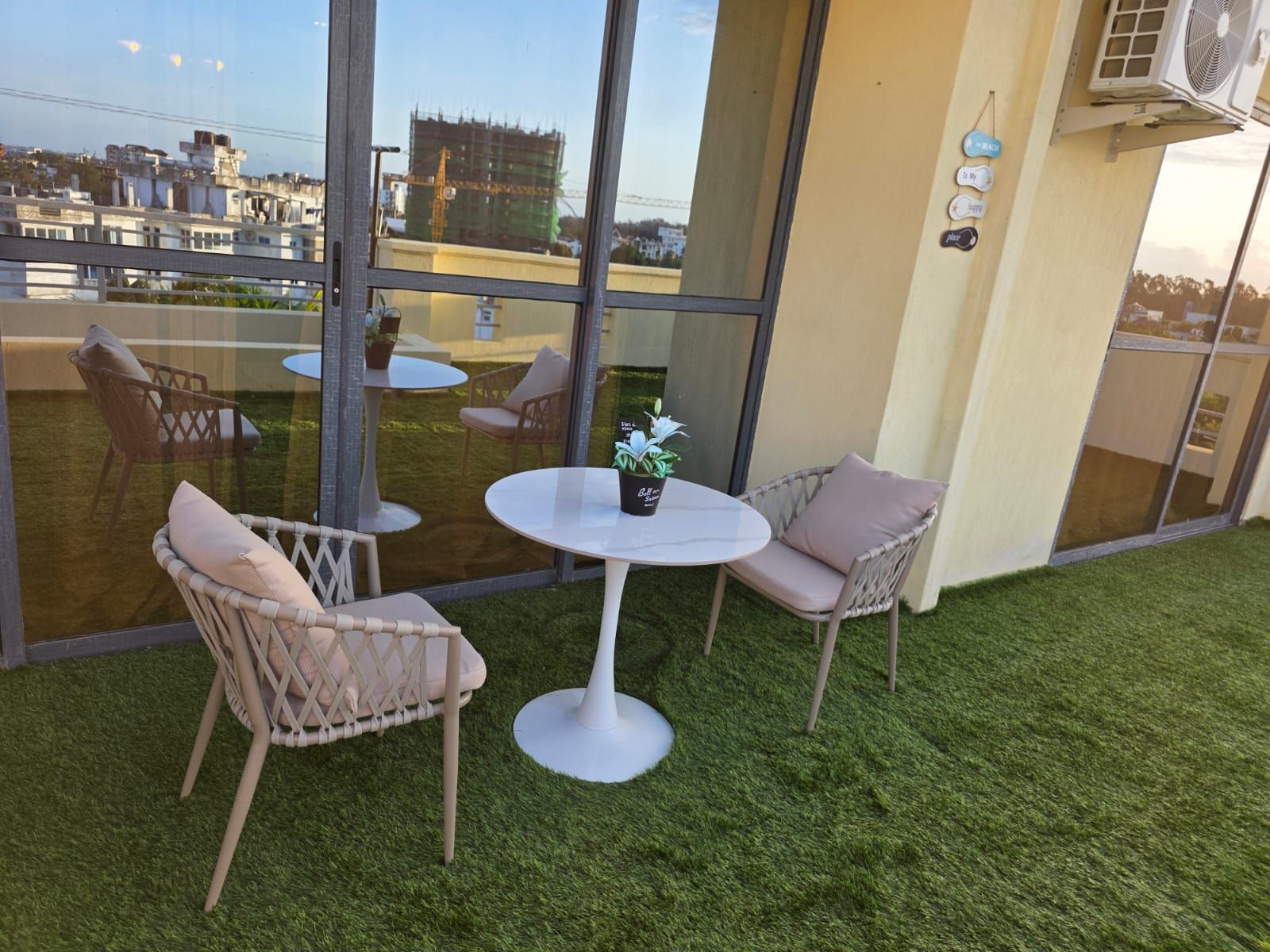 A balcony with artificial grass, two wicker chairs, a small round table, and a potted plant.