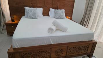 A neatly made bed with a wooden headboard, two bedside tables with lamps, and a patterned rug on the floor.