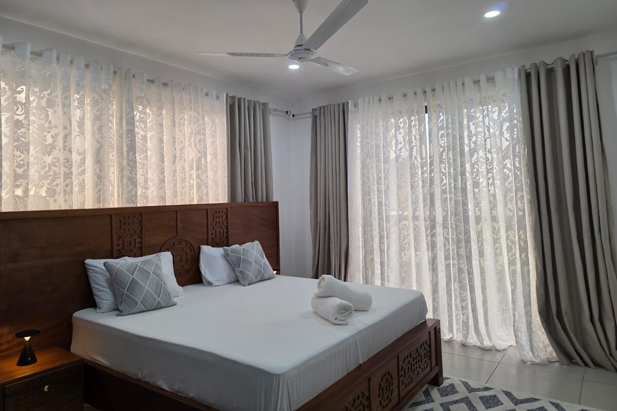 A bedroom with a bed, curtains, a ceiling fan, and a nightstand.