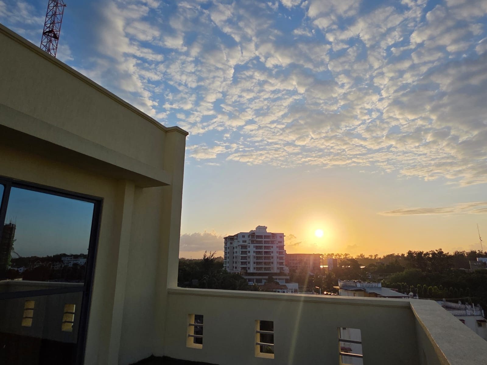 A building with a flat roof, a large window, and a view of the sunset over a cityscape.