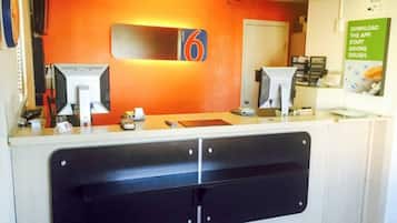 A reception desk with a digital display, a counter, and a door in the background.