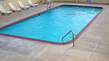A swimming pool with a safety ladder, lounge chairs, and a tiled deck.