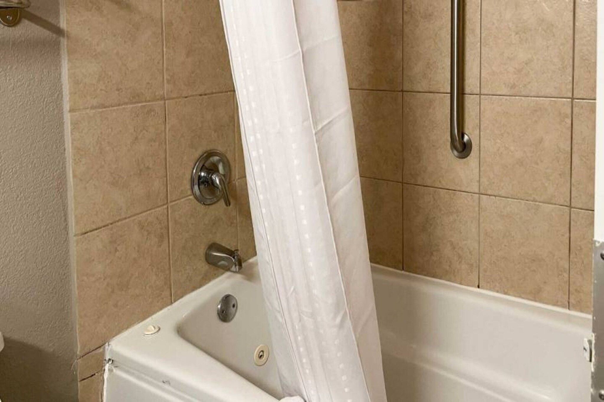 Une salle de bain avec une baignoire, un rideau de douche et une barre d’appui.