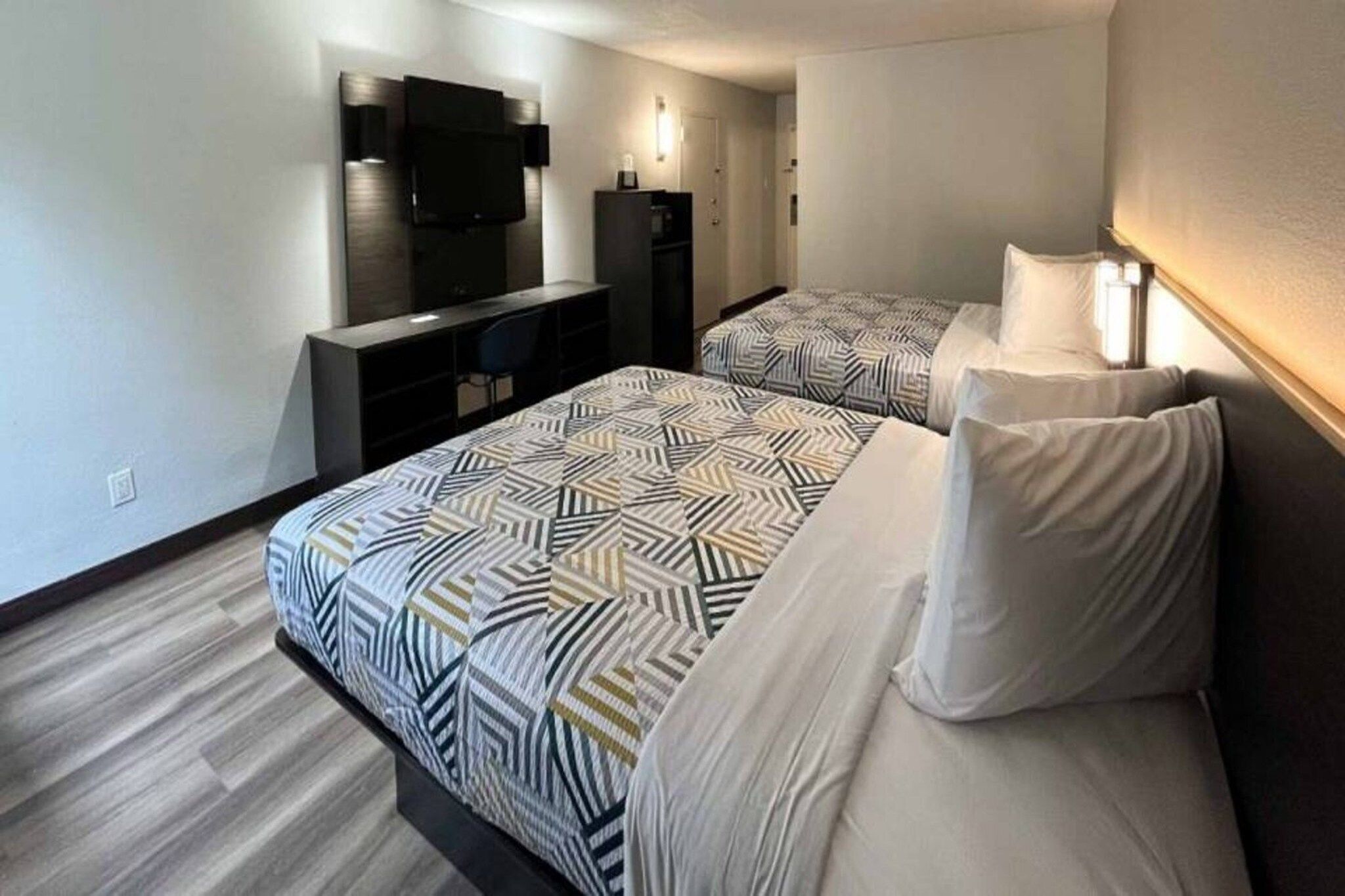 A hotel room with two beds, a desk, a television, and a mirror.