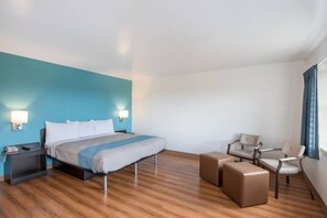 Habitación de hotel con cama, mesitas de noche, escritorio, dos sillas y ventana con cortinas.