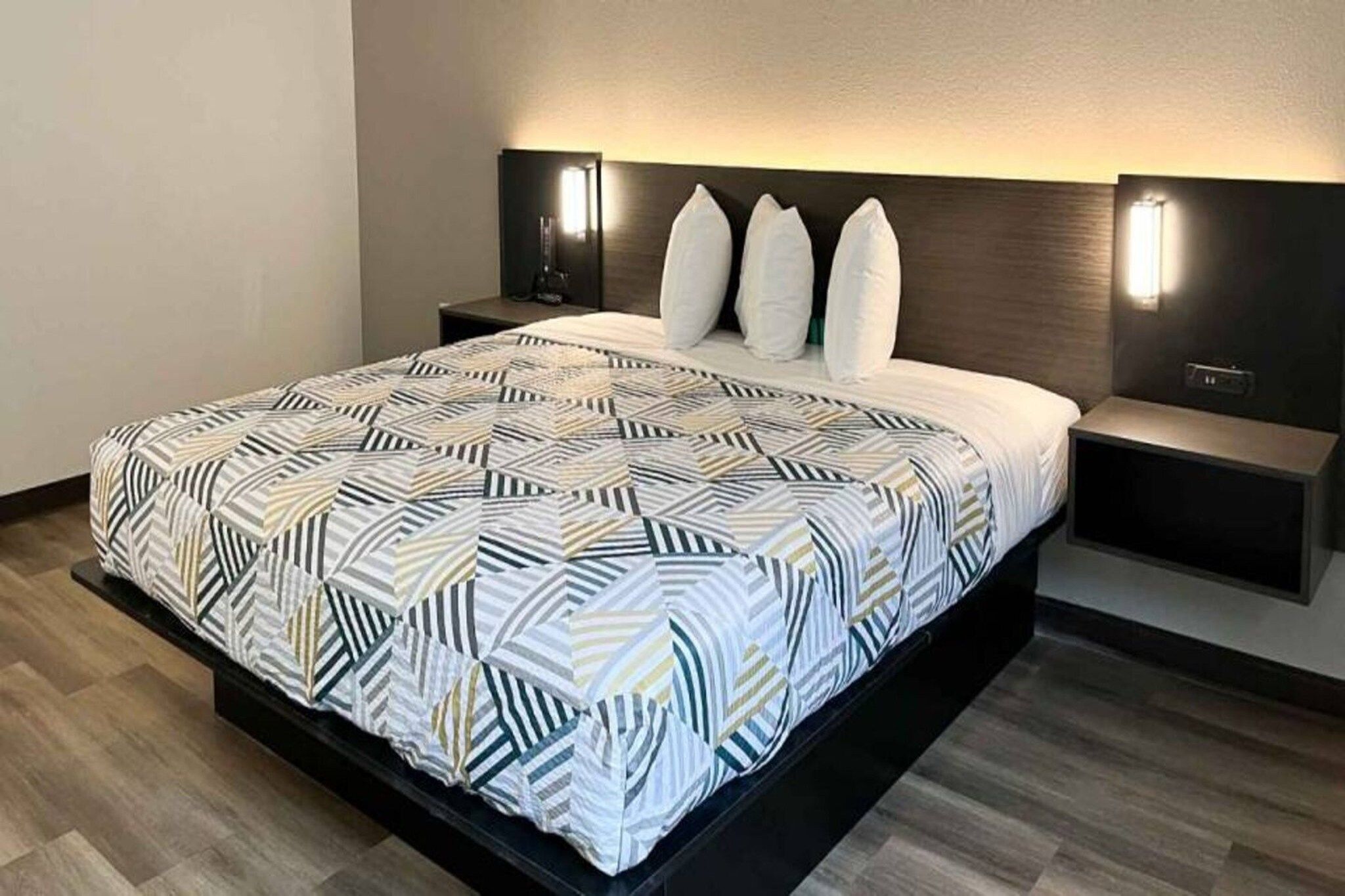 Habitación de hotel moderna con una cama grande, cabecera oscura, dos lámparas de noche y suelo de madera.