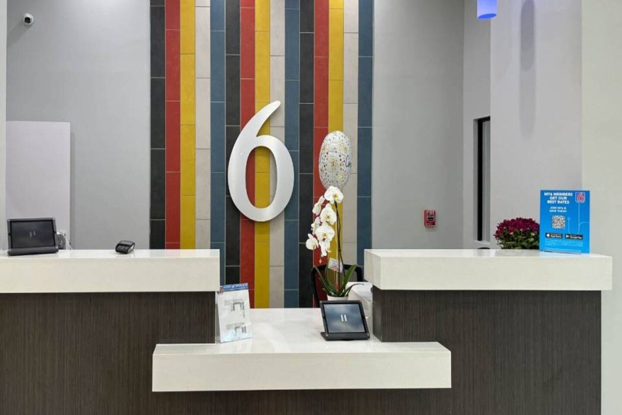 A reception desk with a large number '6' on the wall, a small potted plant, and a blue informational sign.