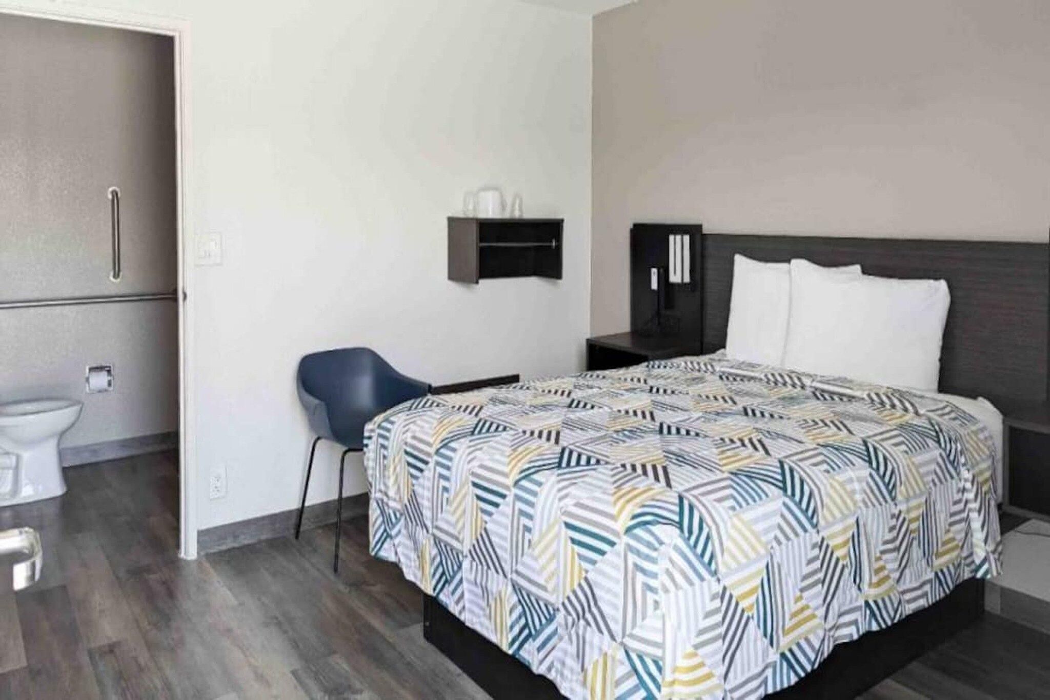 Ett hotellrum med en säng, en stol, ett litet bord, en garderob och en toalett.