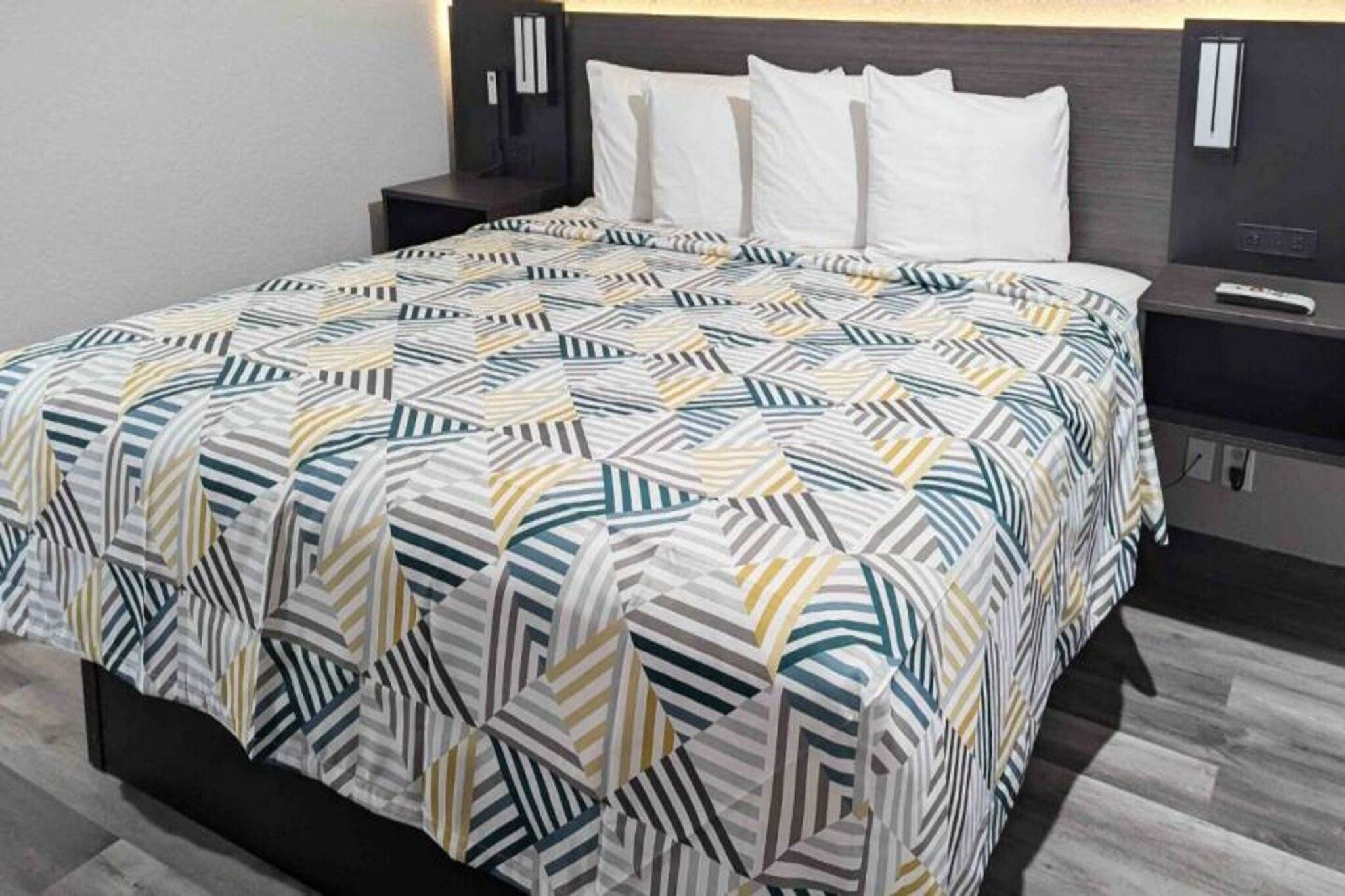 A neatly made bed with a patterned bedspread, a bedside table with a lamp, and a wall-mounted TV.