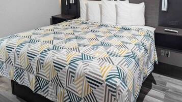 A neatly made bed with a patterned bedspread, a bedside table with a lamp, and a wall-mounted TV.