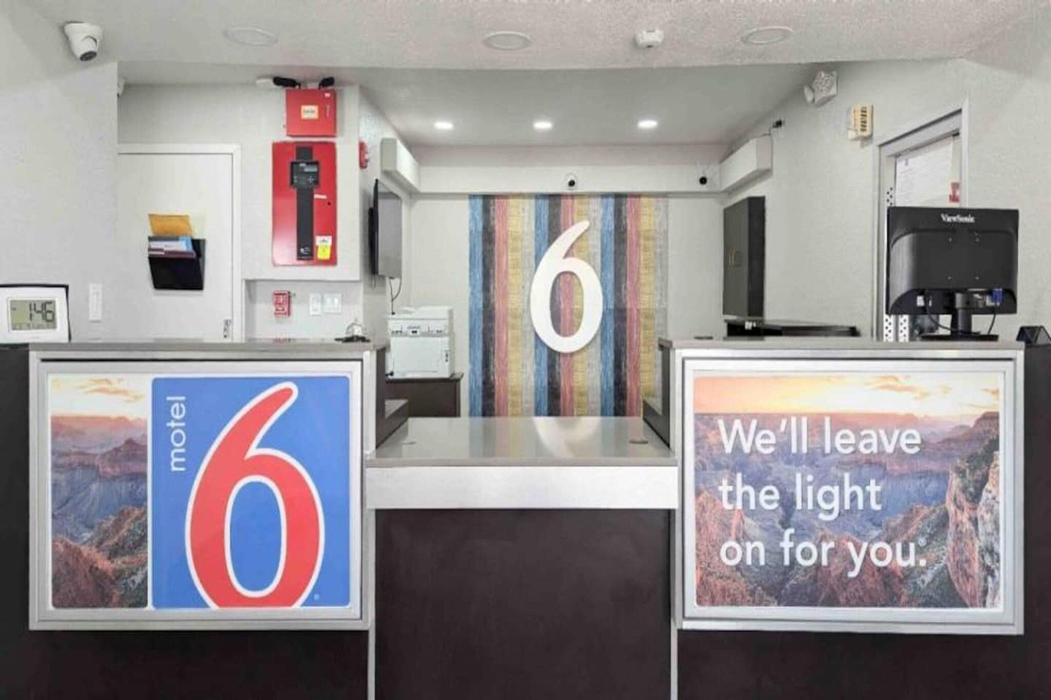 A motel reception desk with a large number '6' and a sign that says 'We'll leave the light on for you.'