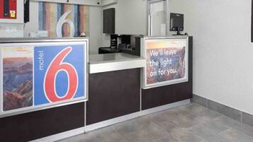 A hotel reception desk with a large number '6' sign, a computer monitor, and a sign with a sunset view.