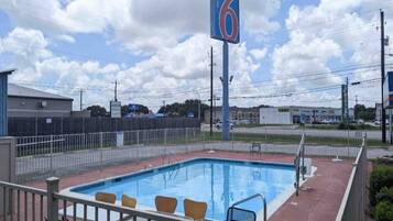 A motel with a swimming pool, a fenced area, and a clear sky.