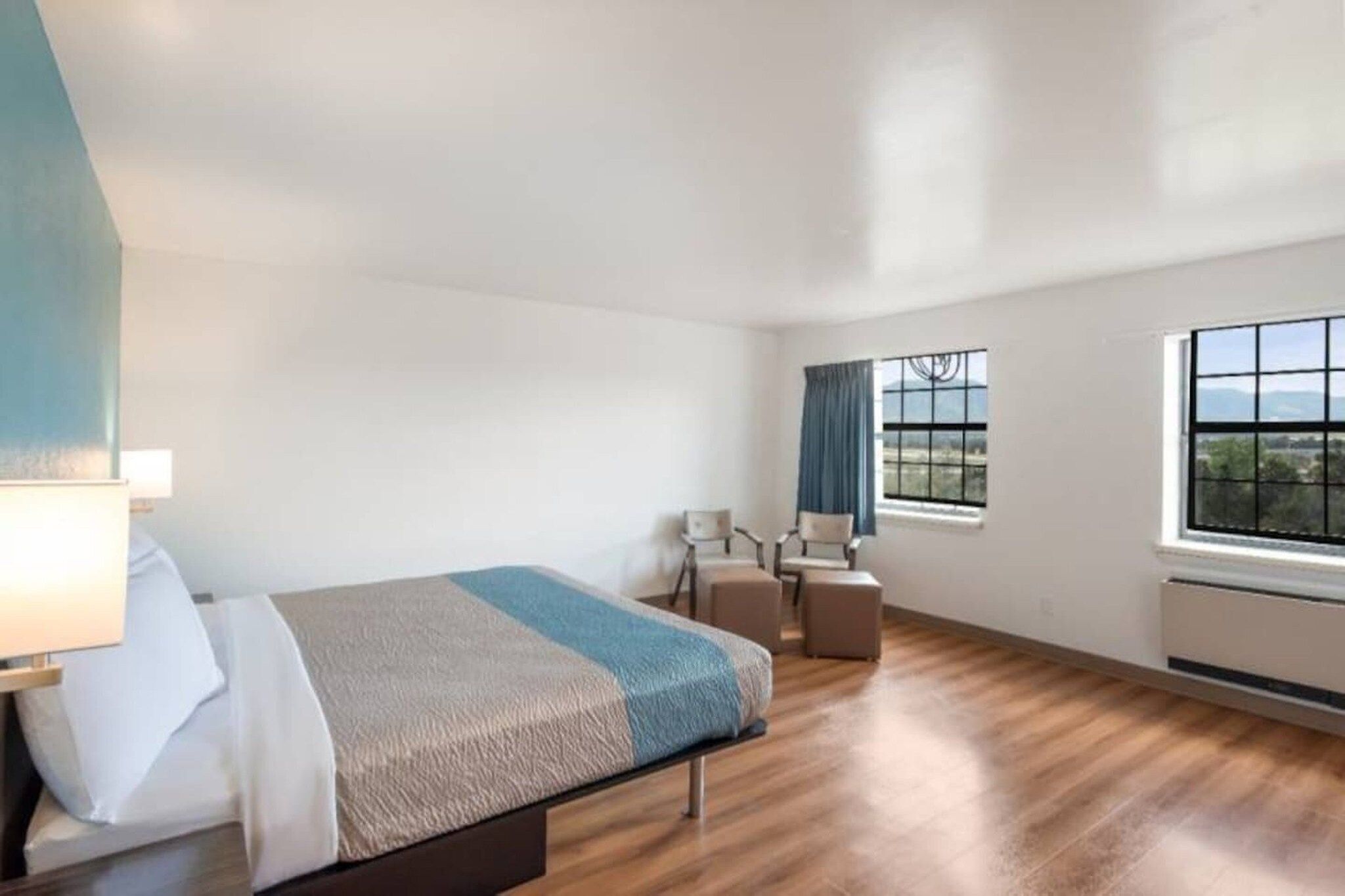 A hotel room with a bed, a desk, a chair, and a view of the outdoors through the window.