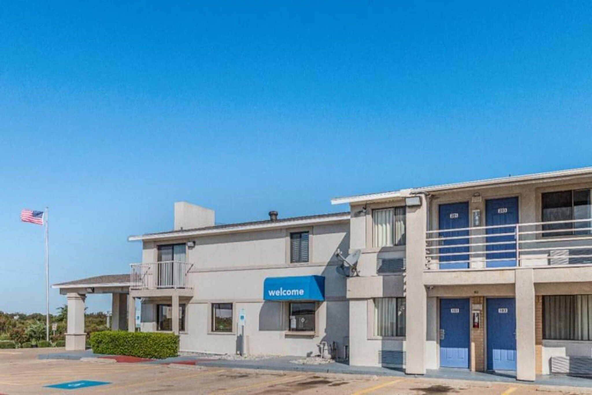 A building with a 'welcome' sign, a flag, and a parking lot.