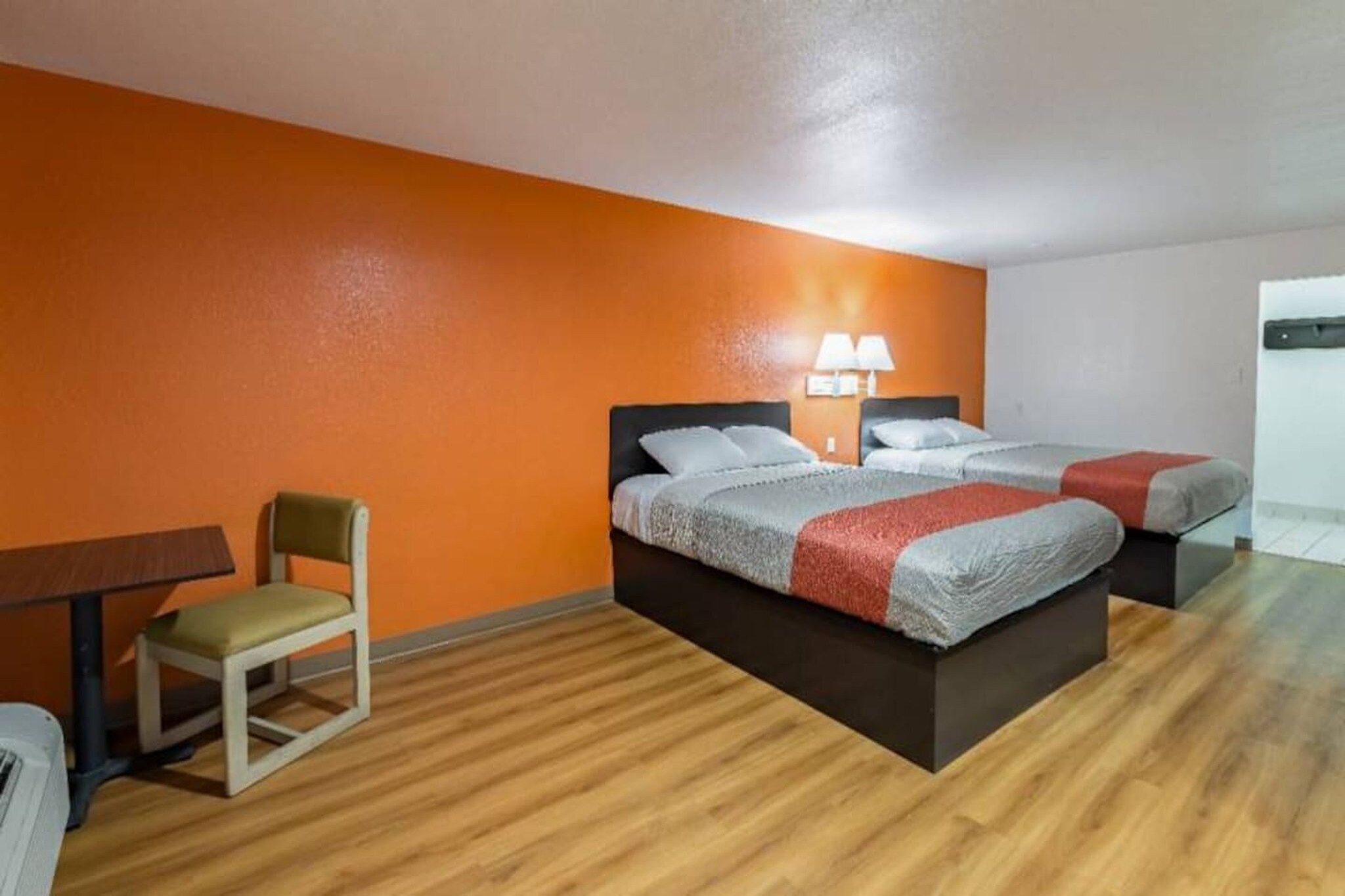 A hotel room with two beds, a small table, a chair, and a lamp.