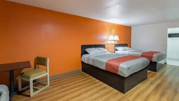 A hotel room with two beds, a small table, a chair, and a lamp.