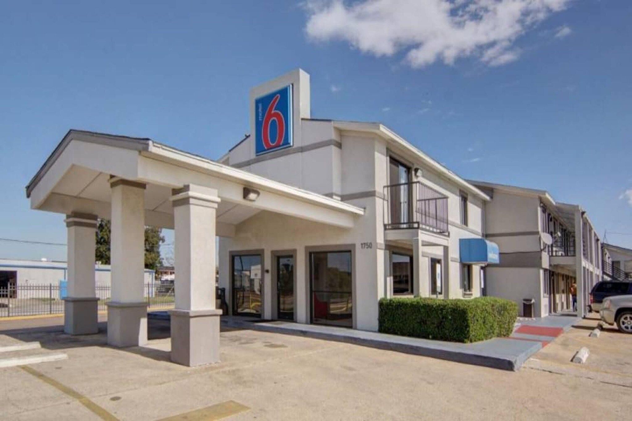 Et moderne hotel med et markant logo med nummeret '6', en overdækket indgang og et tydeligt synligt adressenummer.