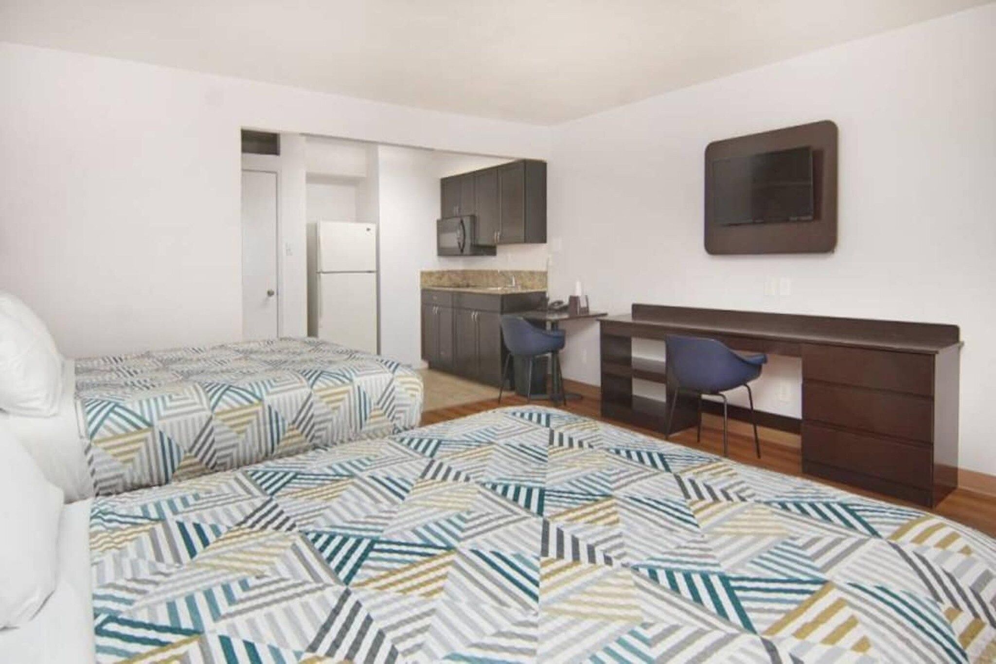 Une chambre de taille modeste comprenant deux lits, un coin cuisine et un bureau avec des chaises.