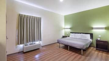 A hotel room with a bed, bedside tables, a heater, and a window with curtains.