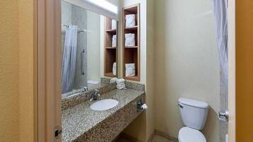 A bathroom with a granite countertop, two sinks, a toilet, a shower, and a mirror.