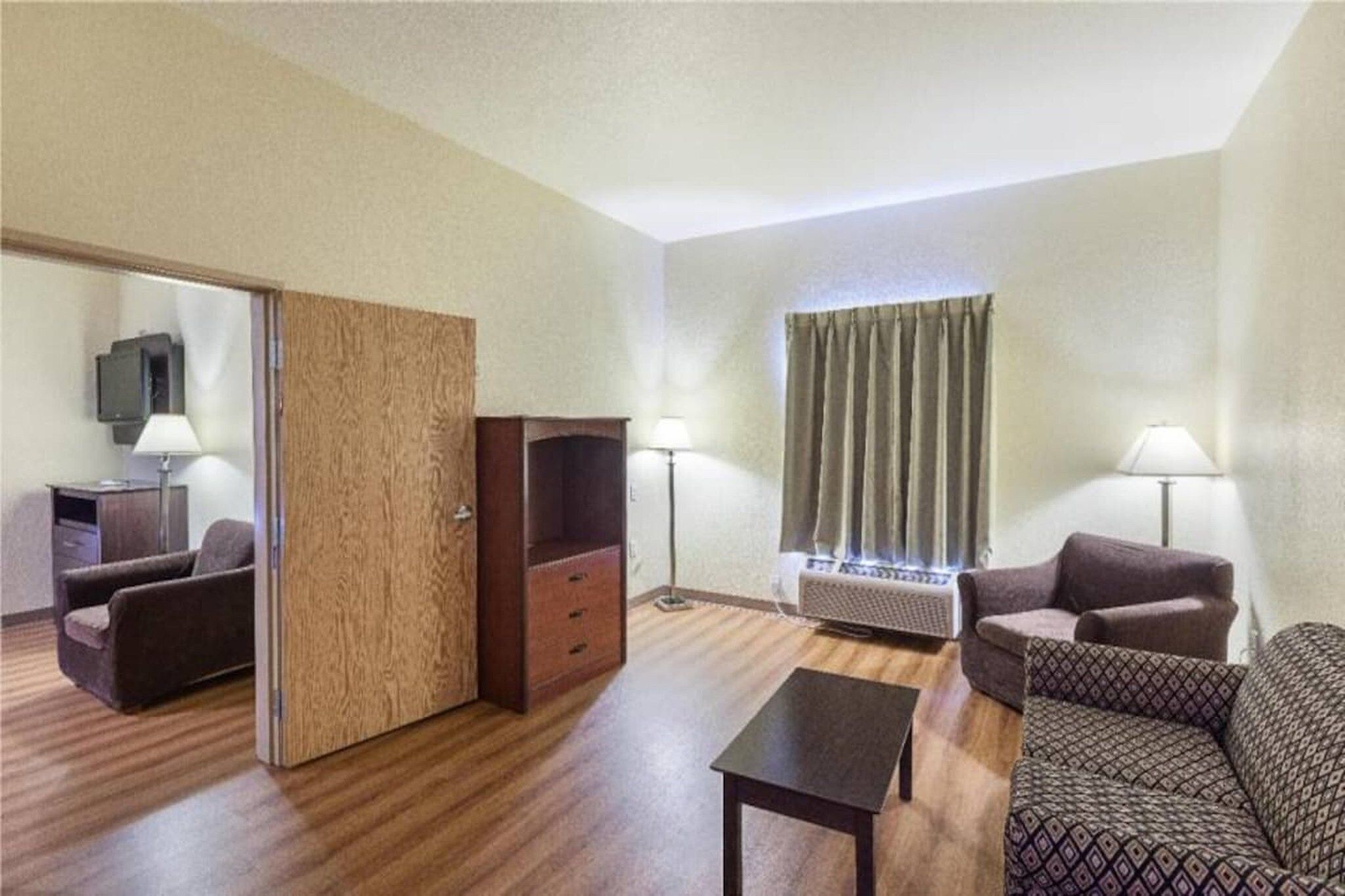 A hotel room with a sofa, a coffee table, a TV, and a window with curtains.