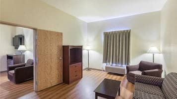 A hotel room with a sofa, a coffee table, a TV, and a window with curtains.