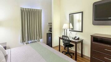 A hotel room with a bed, a desk with a chair, a dresser, a mirror, and a television on the wall.