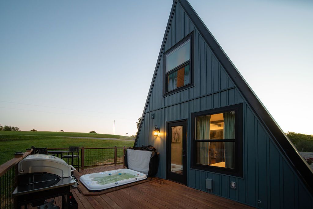 A modern, triangular-shaped building with a deck area featuring a hot tub and barbecue grill.