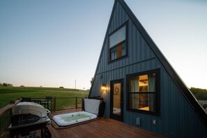 A modern, triangular-shaped building with a deck area featuring a hot tub and barbecue grill.