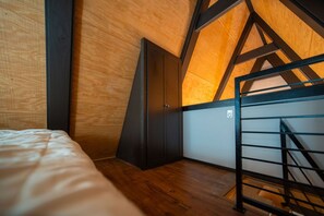 A bedroom with a sloped ceiling, wooden flooring, a bed, a wardrobe, and a metal staircase.