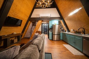 A cozy attic space with a sofa, kitchenette, and a staircase leading to another level.