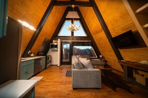 A cozy attic bedroom with a sloped ceiling, a built-in desk, a comfortable sofa, and a large window offering a view.